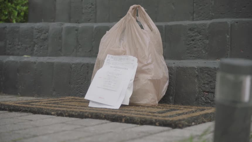 Person wearing gloves places delivery and paperwork on rug against steps