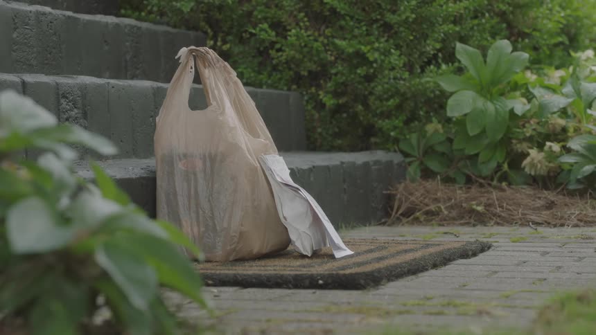 A woman wearing gloves drops off a grocery bag and a prescription bag on a neighbors welcome mat