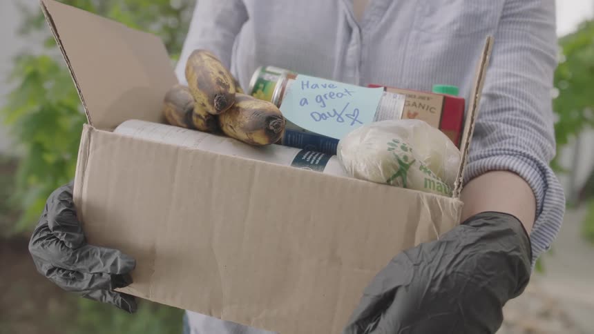 Woman wearing gloves hold carboard box with groceries for delivery