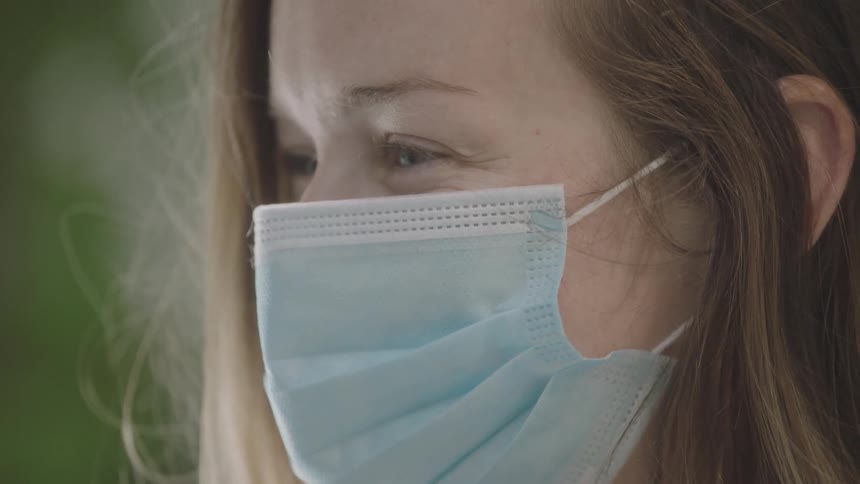 A woman with a mask on lifts her head up and looks forwards