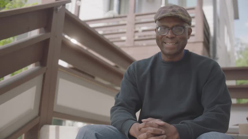 A black man sits on steps outside a house and smiles