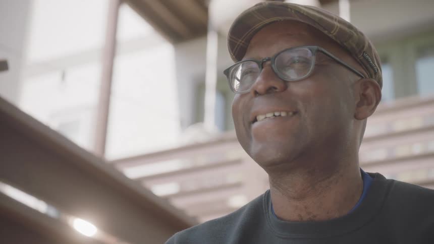 A black man sits outside a house and smiles