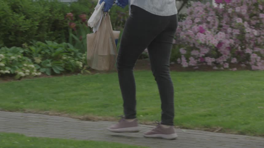 Woman wearing a face mask leaves food bags on the doormat in front of the house during lockdown due to the coronavirus