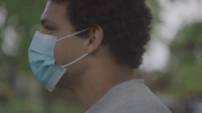 A teenager wearing a mask stands outside