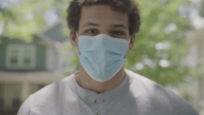 Man wearing a face mask raises his head and looks at the camera in the neighborhood