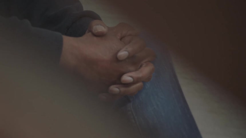 Clasped hands rest on a leg wearing jeans