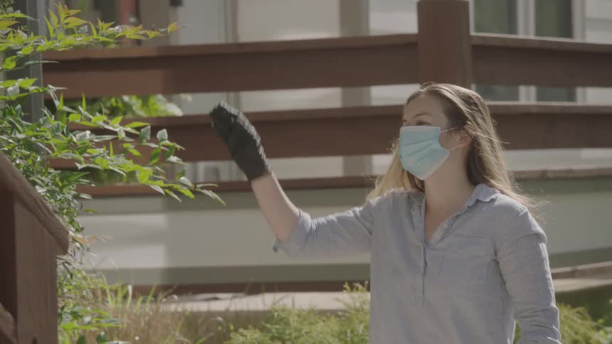 Woman wearing a face mask delivers food bag and waves at the person from a distance during lockdown due to the coronavirus
