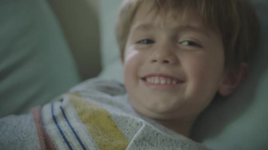 Little boy smiles and waves as he lays on a cushion