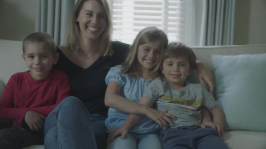 Woman and children sit in group on couch smiling and hugging