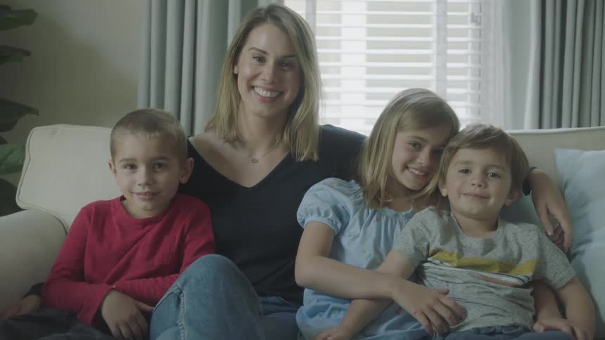 Mother and her three children sit on the couch smiling while posing for their picture to be taken
