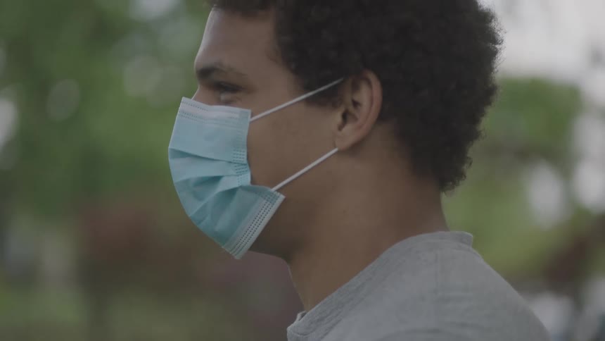 A man wearing a medical mask stands outside in a yard