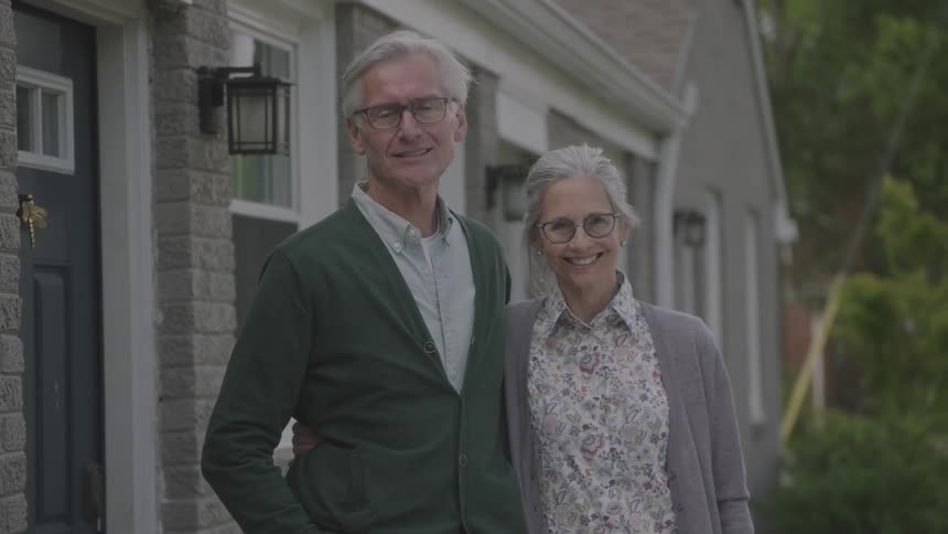 A couple standing outside their home laugh and hug