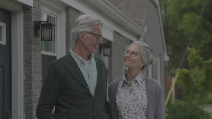 Older couple stand outside house taking time to exchange glances