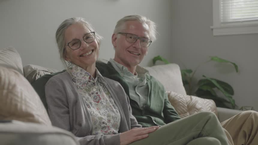 Elderly man and woman sitting on the sofa smiles happily in the living room at home
