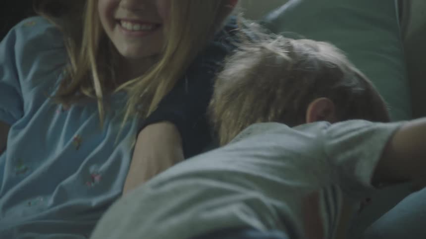 A family sits on a sofa while laughing and hugging each other