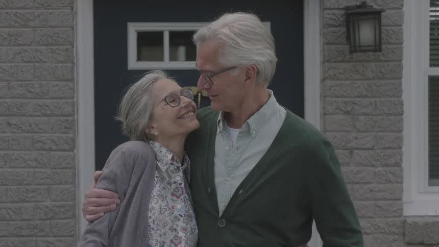 Elderly husband and wife hugging and smiling on front porch