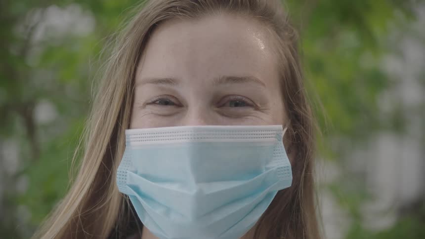 Blonde woman wearing a surgical mask looks at the camera as the breeze blows her hair