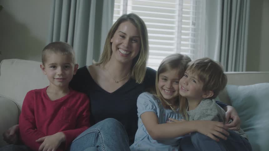 Woman and three children sit on a sofa and smile for the camera