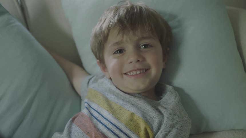 Child lying down on the sofa comfortably looks at the camera and smiles broadly