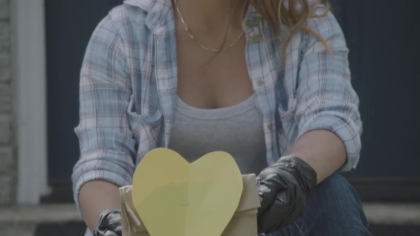 Asian girl wearing a face mask sitting on front steps holding a paper bag with a yellow heart