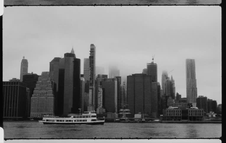 A ferry and boats travel in the water with a city skyline behind on a foggy day
