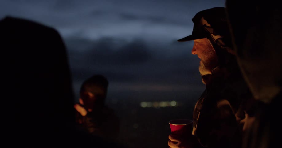A woman gestures as she talks and her friends laugh as they stand outside by a fire