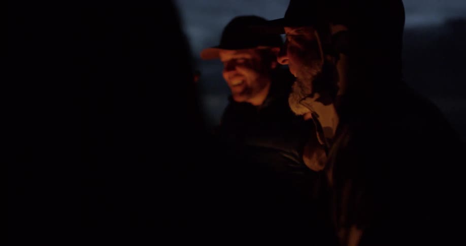 A group of friends laugh while standing around a bonfire outside