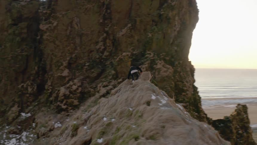 A man pauses on a rocky ridge overlooking the ocean before starting to climb down