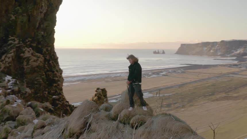 A man stands on a cliff at the beach