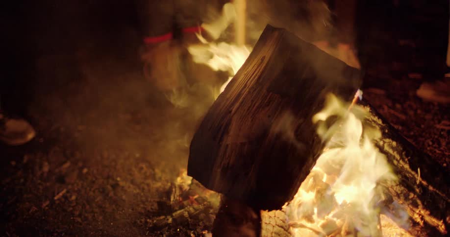 Close up of wood piece burning in a bonfire surrounded by people