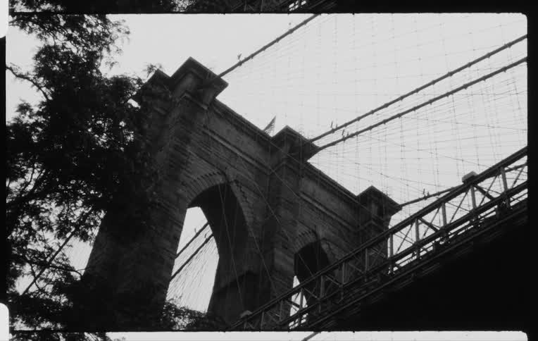 The american flag on top of a cable suspension bridge waves in the wind