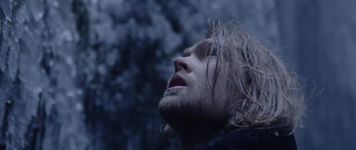 A man standing outdoors near an icy wall while snow falls behind him