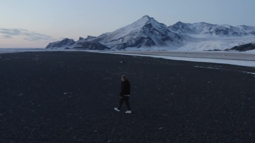 Man walks across the coast and snow covered mountains on the background