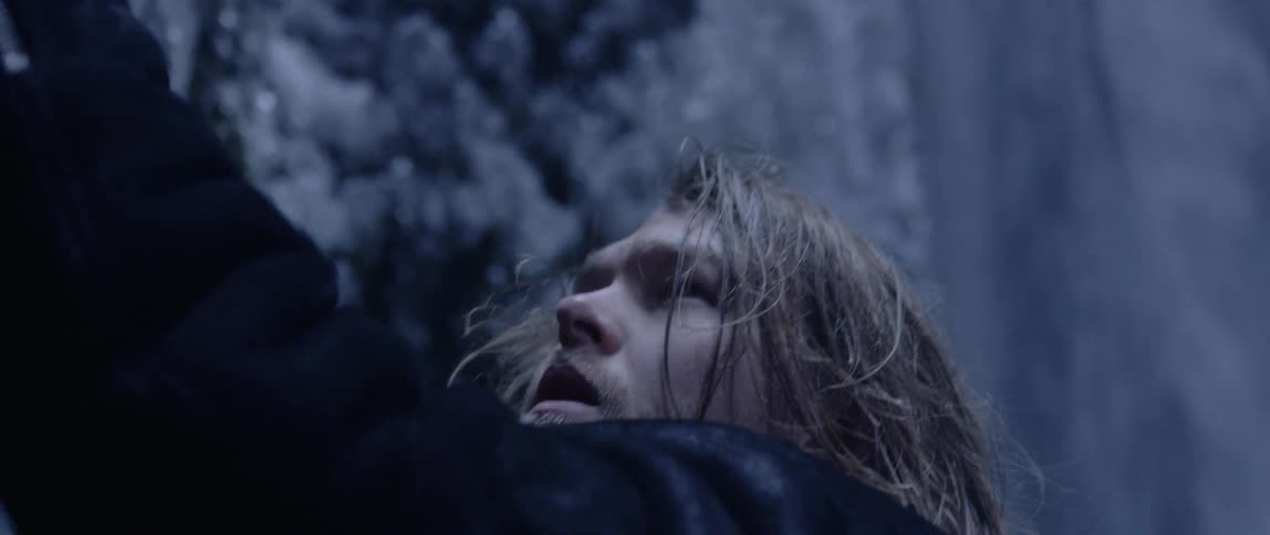 A man reaches and struggles against a rock wall near a waterfall