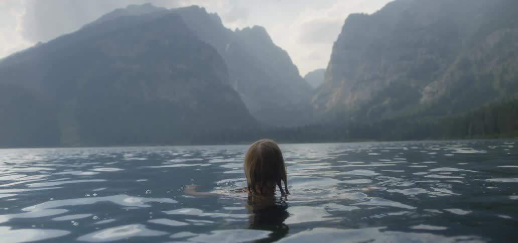 A woman swimming in a body of water at the base of low mountains