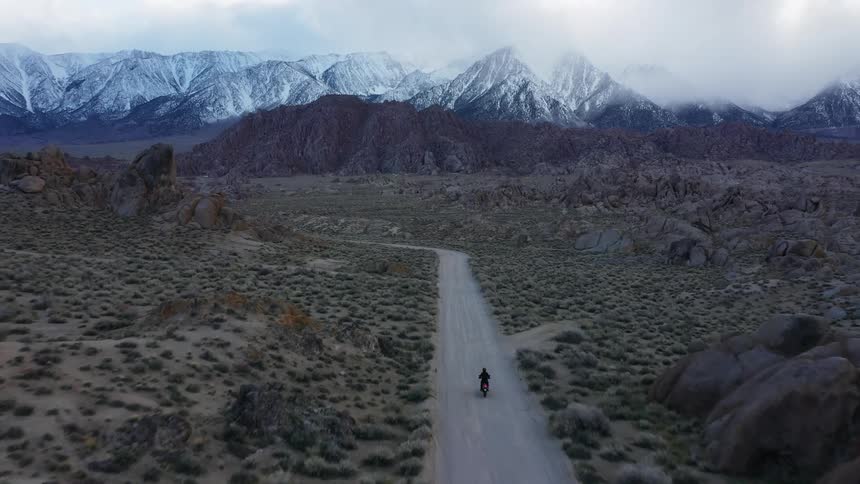 A person drives a motorcycle down a road towards the mountains