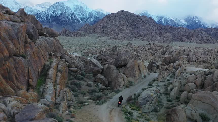 A motorcyclist rides through a winding road towards snow capped mountains