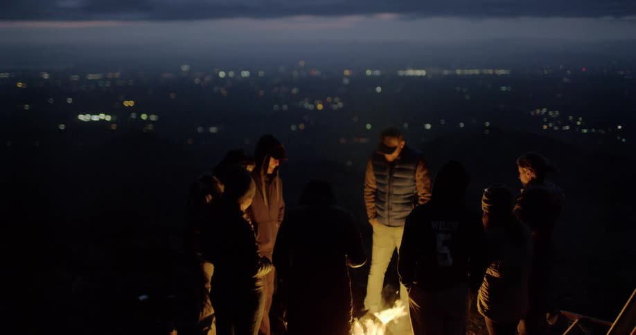 Group of friends gather around bonfire at night
