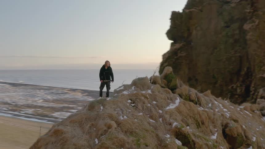 A person stands on top of a large ocean coastal mountain cliff