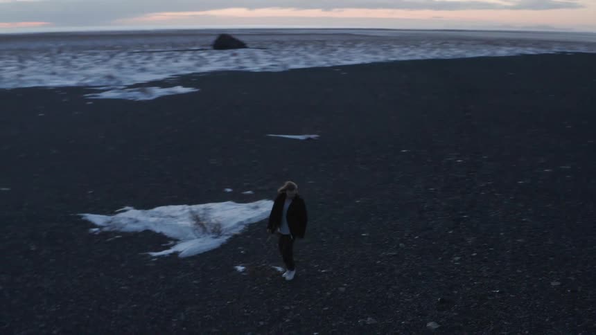A person walks on a black sand beach in the winter