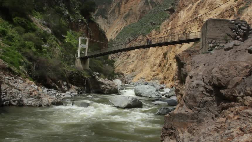 View of a bridge gaping a stream as people travel over it