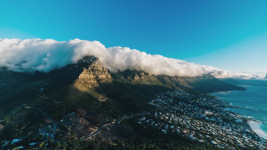 Clouds rolling over mountains that loom over a city on the coast