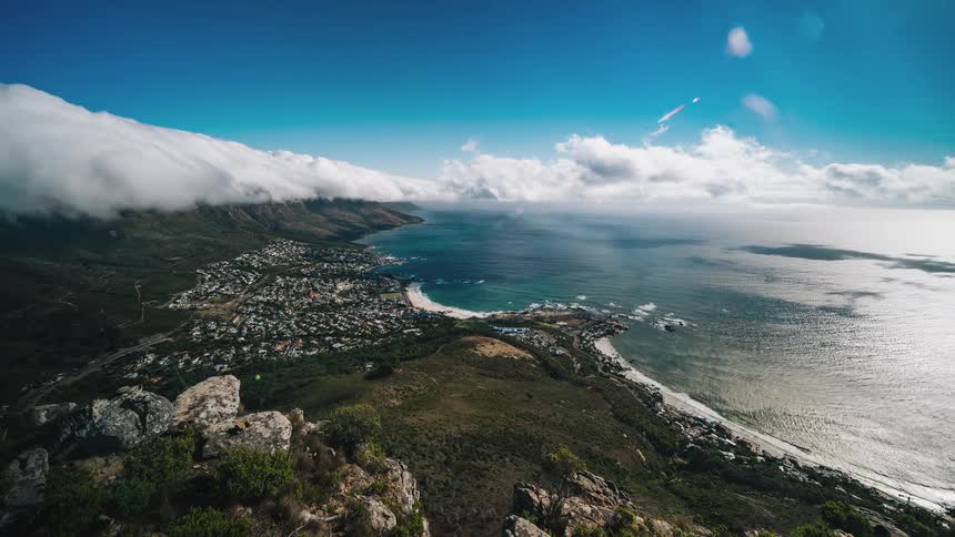 Clouds and water flow past town occupying land between slope and ocean