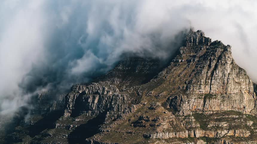 White cloud flows over the slopes of a rocky mountain