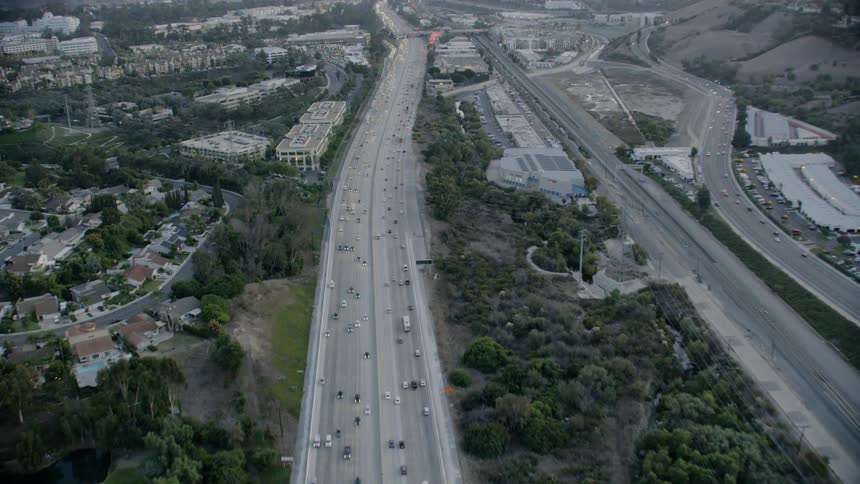 Traffic moves along highway past a golf course neighborhood and commercial buildings