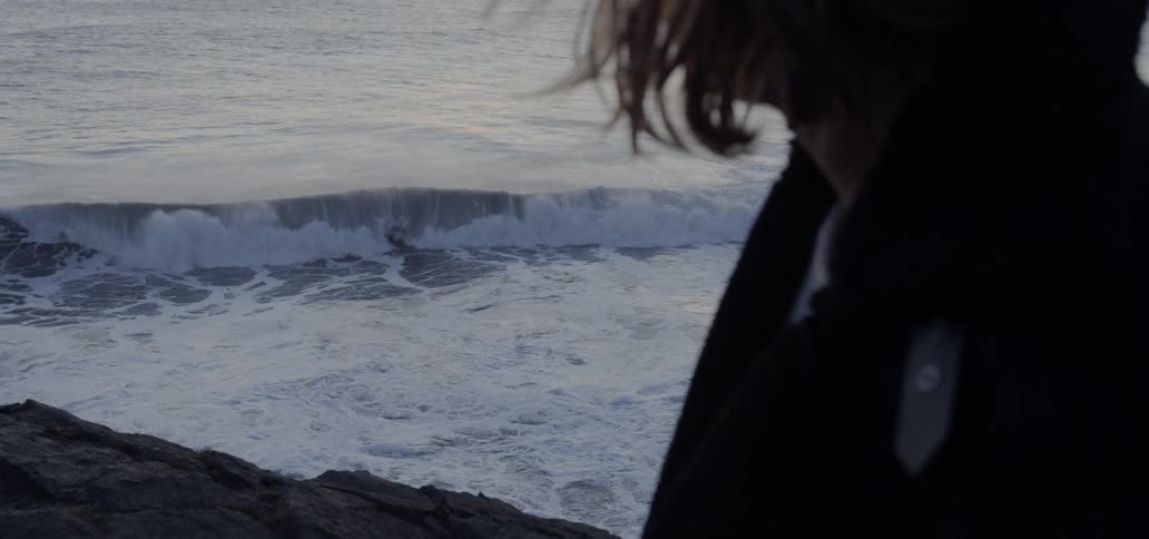 Woman watches foamy waves breaking against the shore