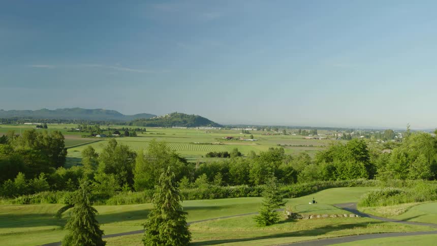 A view of a golf course from the air with farmland and mountains in the background