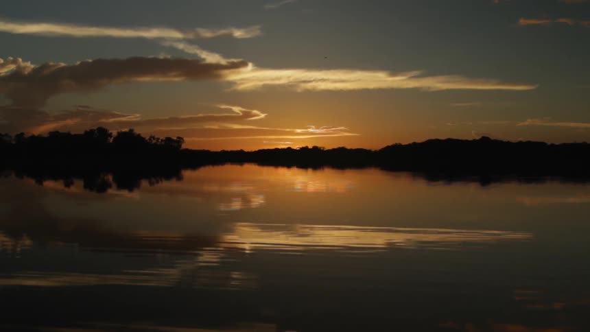 The sun is setting in the distance past the water