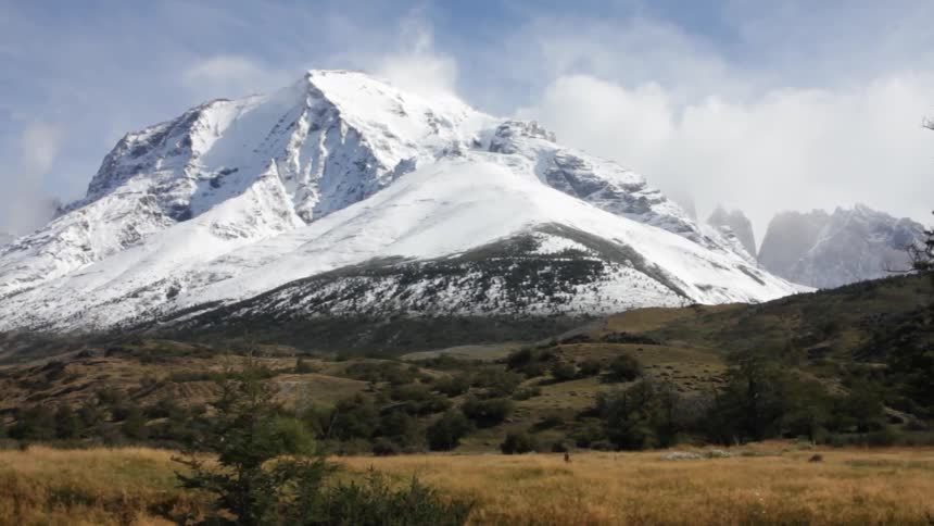 A large mountain covered in snow is seen past a hillside