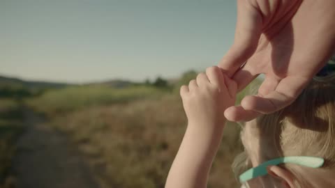 A little girl in sunglasses walking down a path through a field while holding the hand of an adult